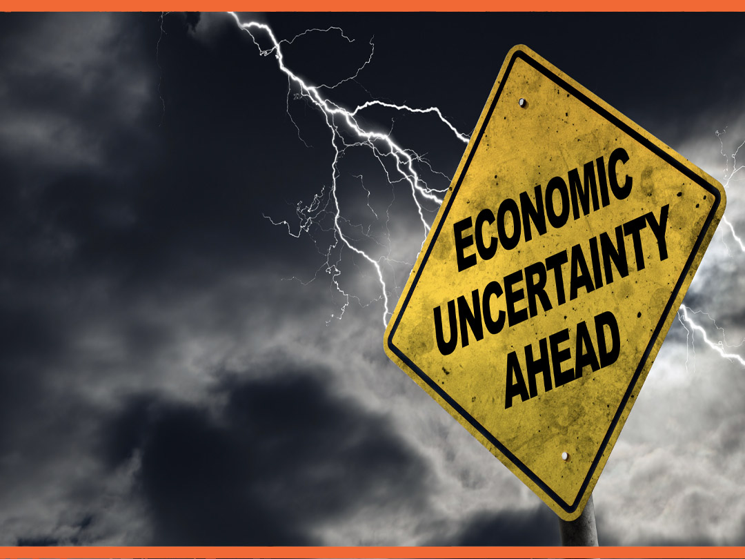 Yellow construction sign reading "ECONOMIC UNCERTAINTY AHEAD" with a lighting storm behind it.