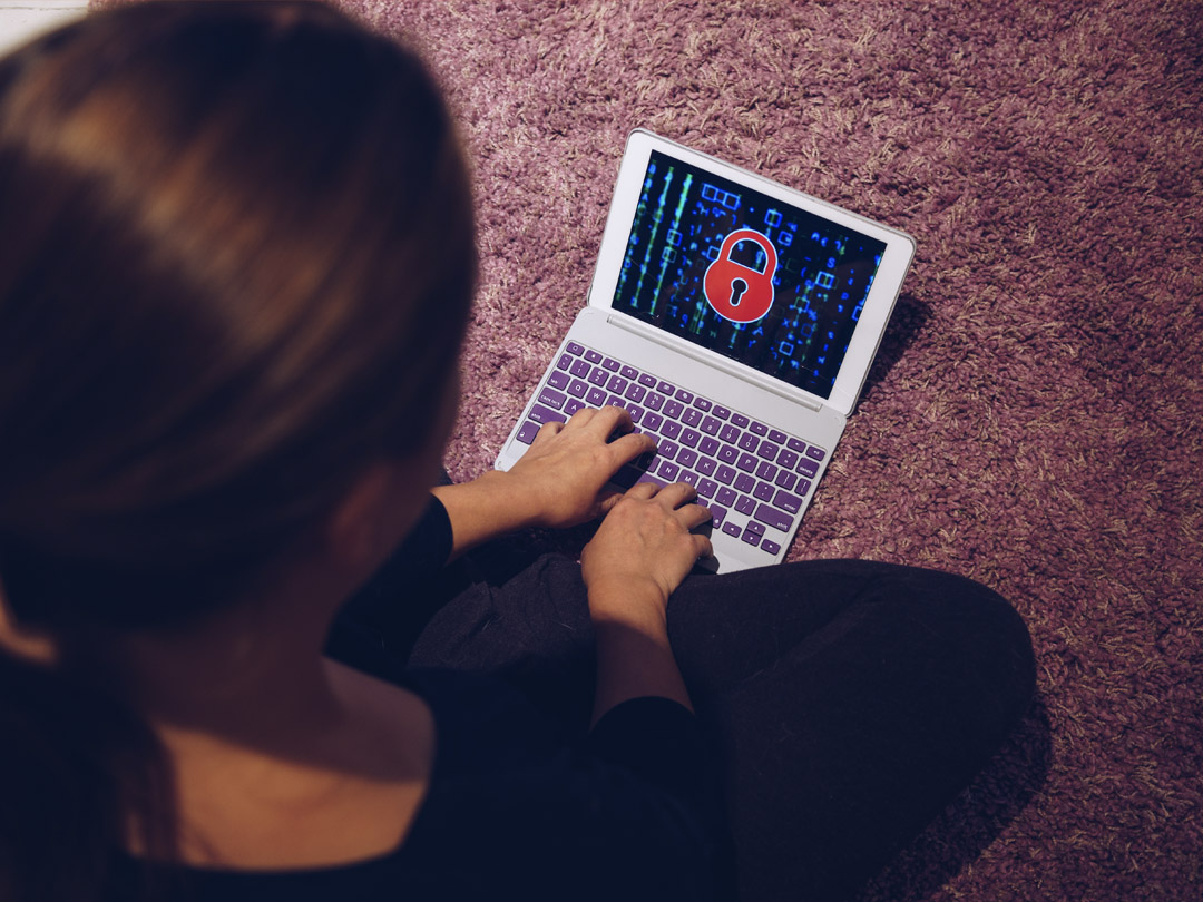 Woman sitting on her carpet using her computer with ransomware on it.